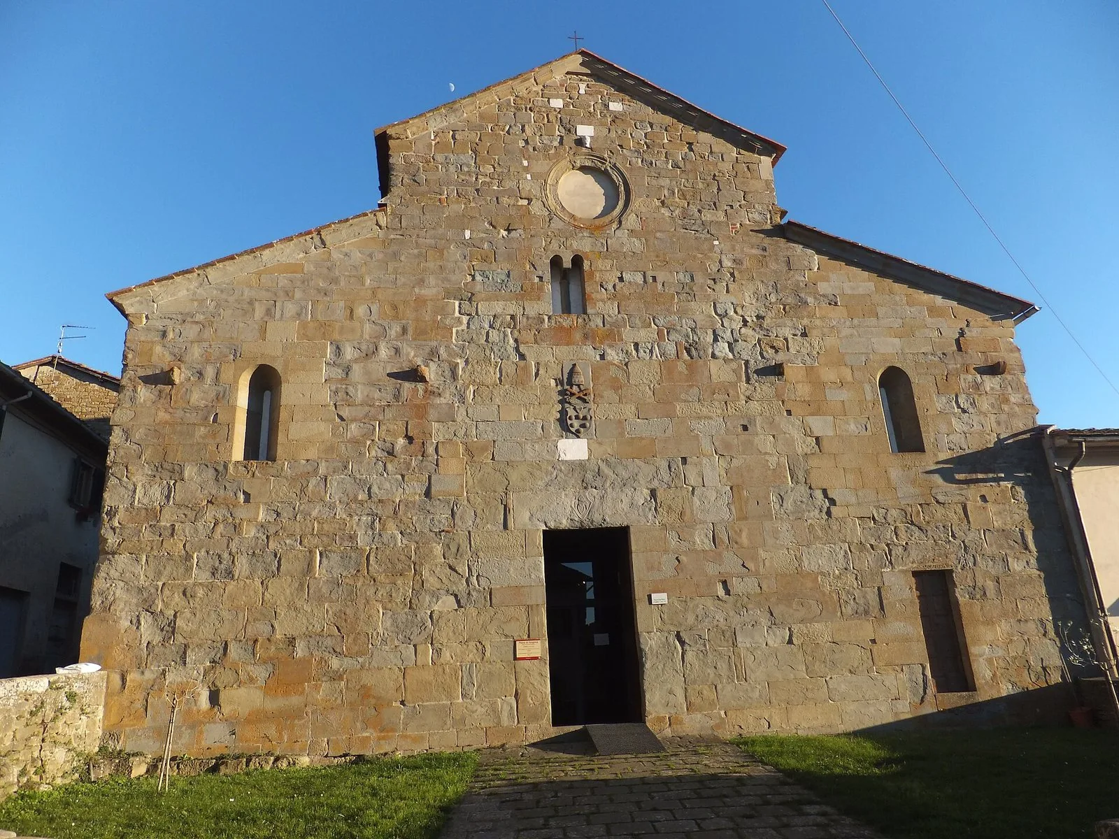 Facciata romanica in pietra della Pieve di San Pietro a Gropina sotto un cielo azzurro